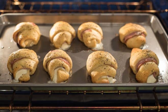 The stuffed crescents baking in the oven on a baking sheet.