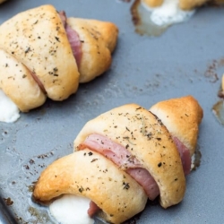 Ham and melted cheese rolled up inside crescent rolls on a baking sheet.