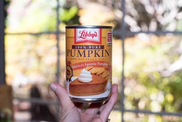 A hand holds up a can of Libby's 100% Pure Pumpkin Puree.