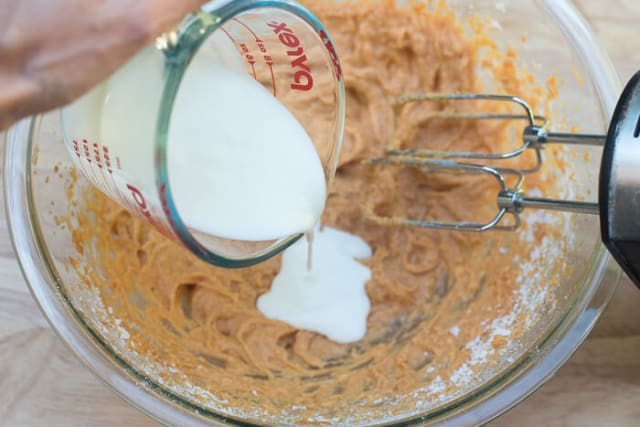 Buttermilk pours from a measuring cup into batter in a bowl.