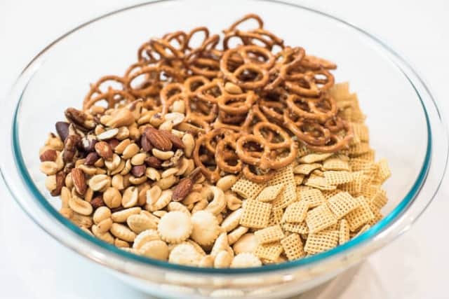 Chex Cereal, twist pretzels, mixed nuts, and oyster crackers in a glass mixing bowl.