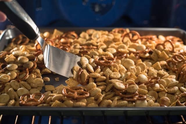 A spatula stirring Garlic Dill Snack Mix on a baking sheet in the oven.