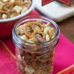 A mason jar filled with Garlic Dill Snack Mix on a bright red napkin.