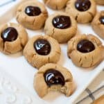 A white tray of peanut butter chocolate thumbprints, one with a bite missing.