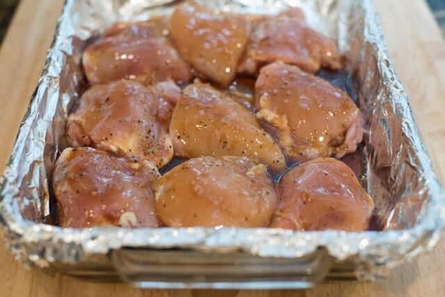 Chicken thighs in a foil-lined baking dish with teriyaki sauce.