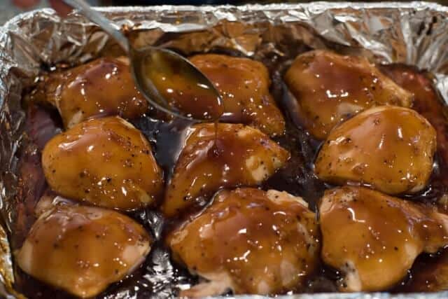 A spoon drizzling teriyaki sauce over chicken in the baking dish.