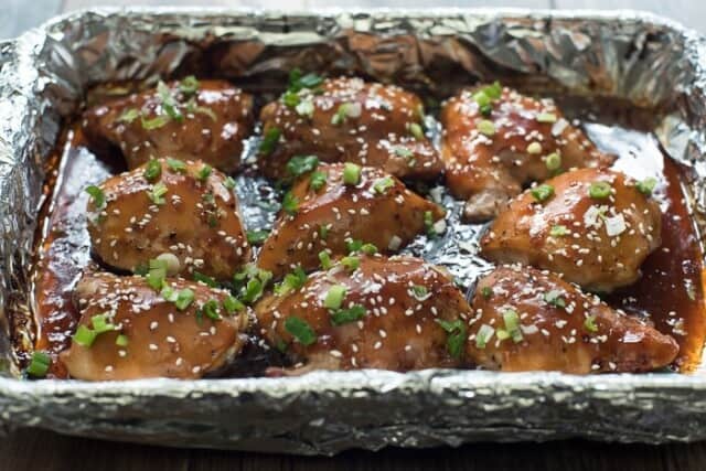 Baked Chicken Teriyaki in a foil-lined baking dish garnished with green onion and sesame seeds.