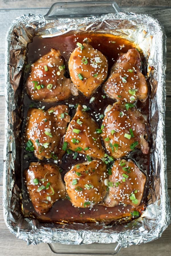  A top down shot of Baked Chicken Teriyaki topped with green onion and sesame seeds in a foil lined baking dish.