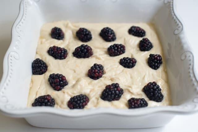 Cake batter topped with blackberries in a square baking dish.