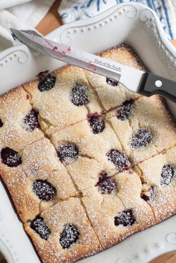 A knife rests over a baking dish of Blackberry Buttermilk Snack Cake after it has been sliced.