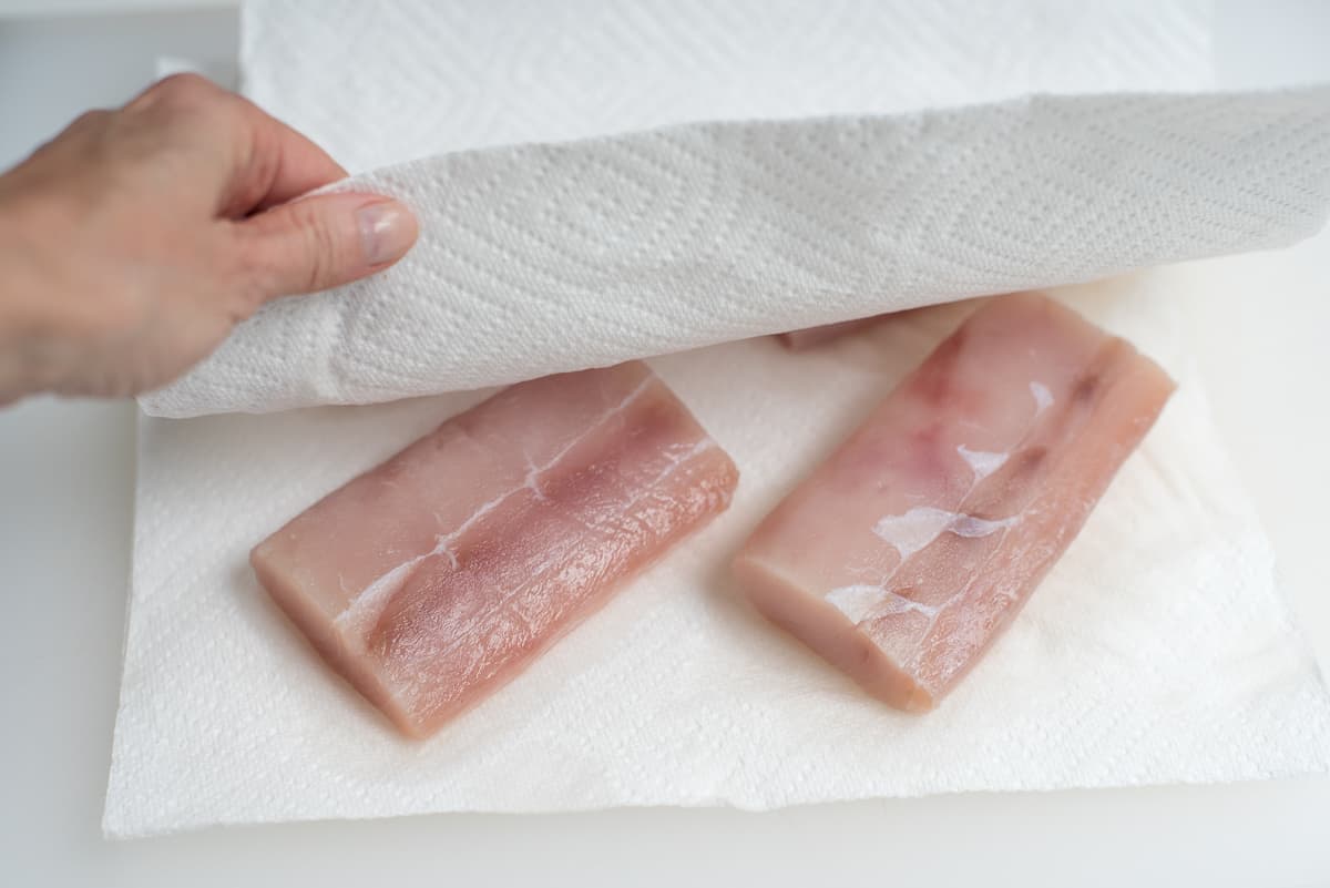 Fish fillets being blotted dry with paper towels.