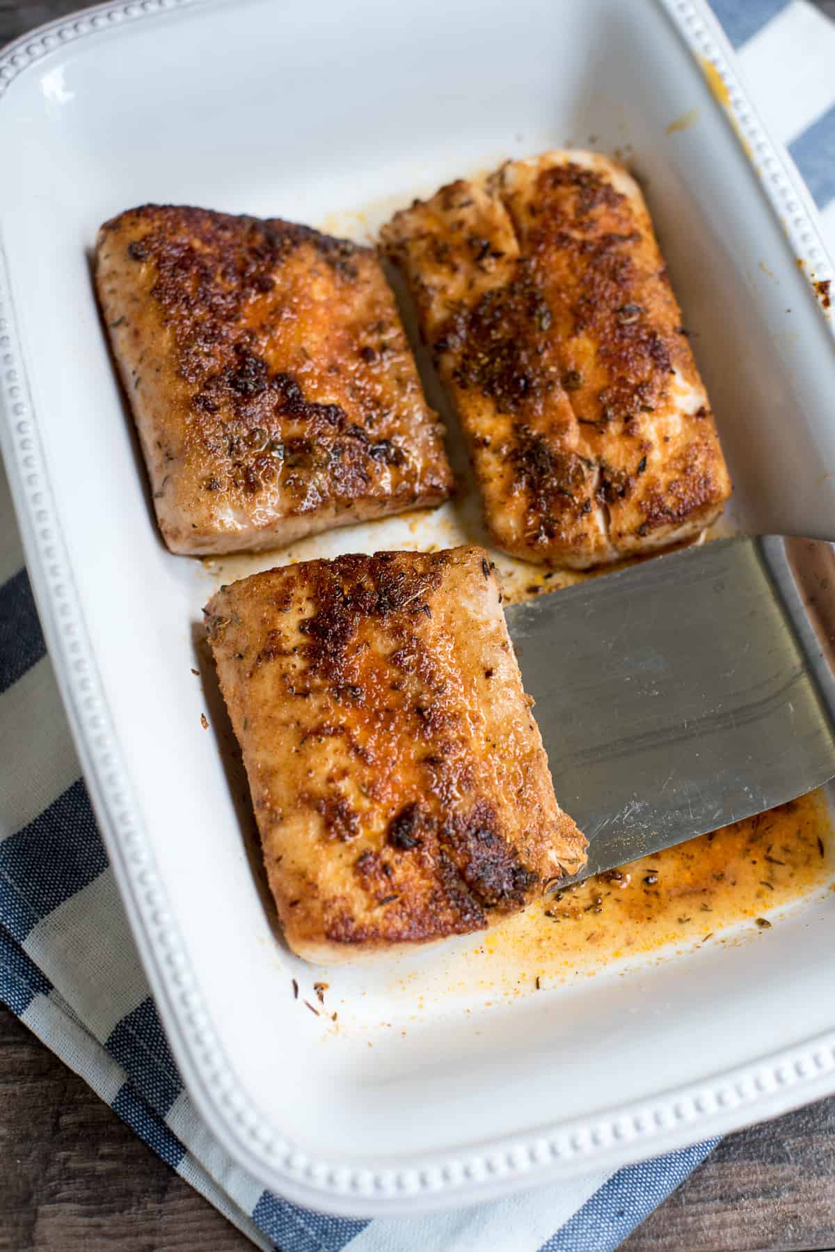 A spatula under a piece of cooked mahi mahi in a serving dish.
