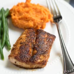 A piece of Blackened Mahi Mahi on a white plate with mashed sweet potatoes and green beans.