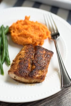 A piece of Blackened Mahi Mahi on a white plate with mashed sweet potatoes and green beans.