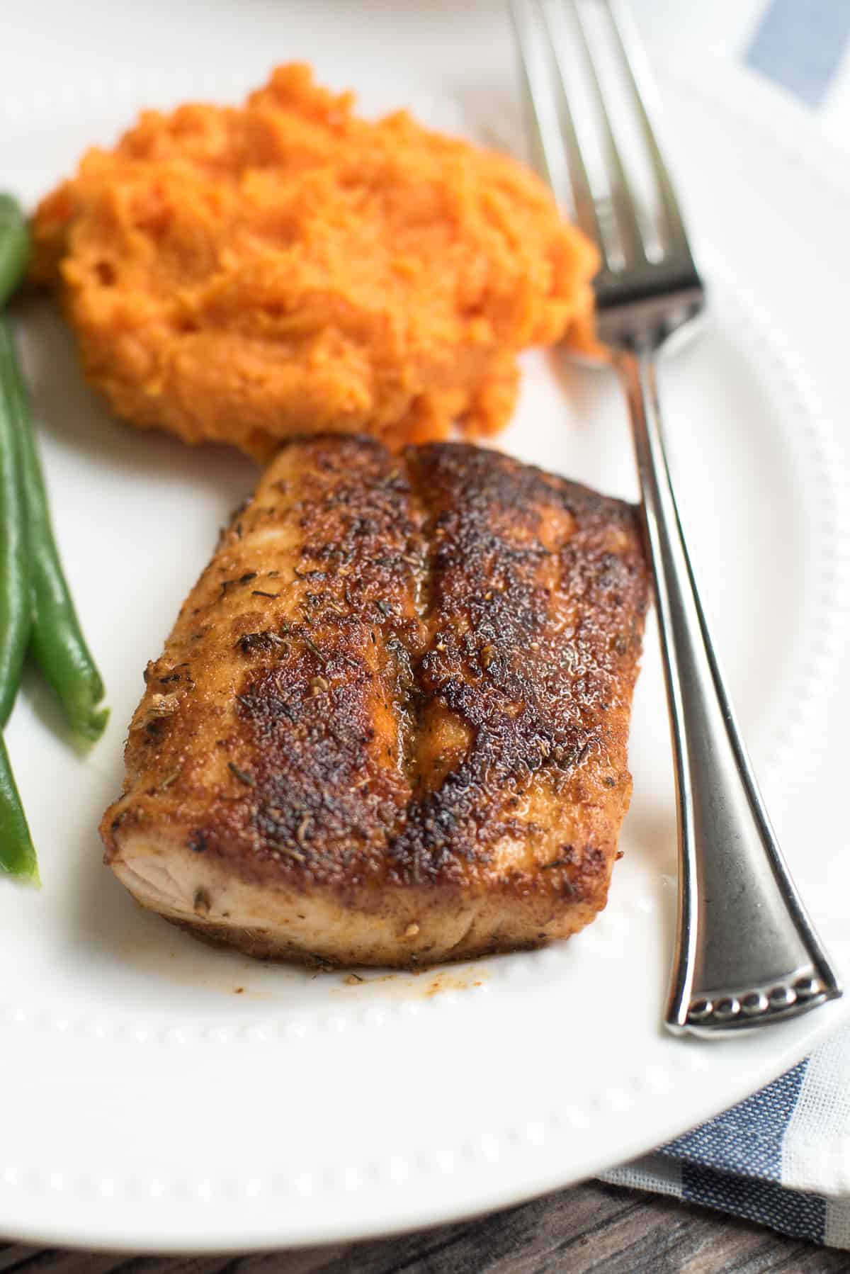 A piece of Blackened Mahi Mahi on a white plate with mashed sweet potatoes.