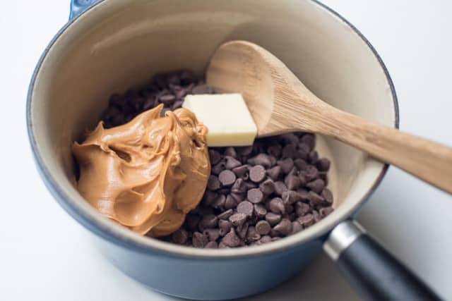 Peanut Butter, chocolate chips, and butter in a blue saucepan with a wooden spoon.