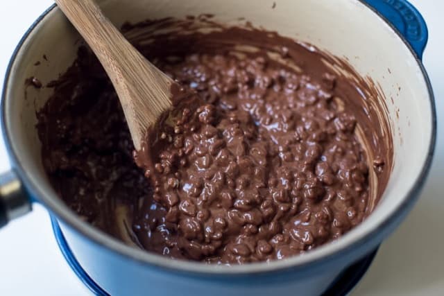 Crisped rice cereal in a  melted chocolate mixture in a blue saucepan.