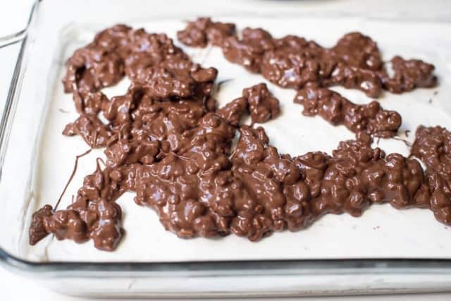 A melted chocolate mixture with rice cereal on top of marshmallow layer in a baking dish.