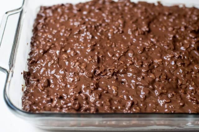 A close up of a crispy rice chocolate layer on top of bars in a baking dish.