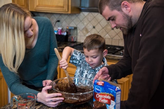 A young man and woman helping a boy stir brownie mix in a bowl.