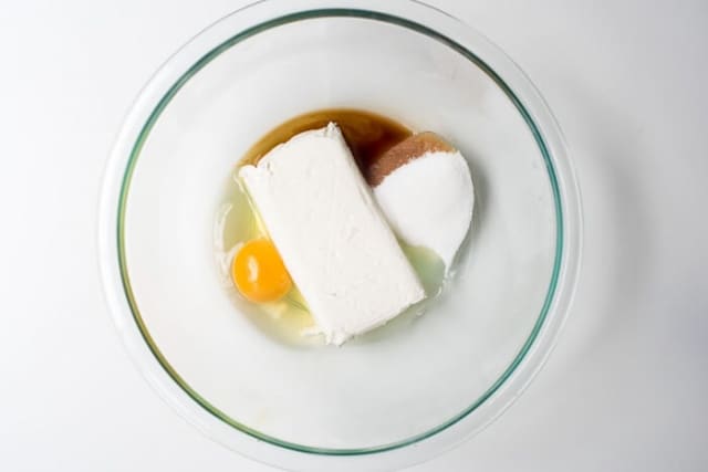 Eggs, sugar, vanilla, and cream cheese in a glass mixing bowl.