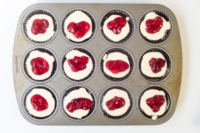 Cherry pie filling on top of a cheesecake mixture in a muffin pan.