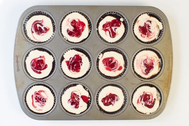 A swirled cherry topping on a cheesecake mixture in a muffin pan.