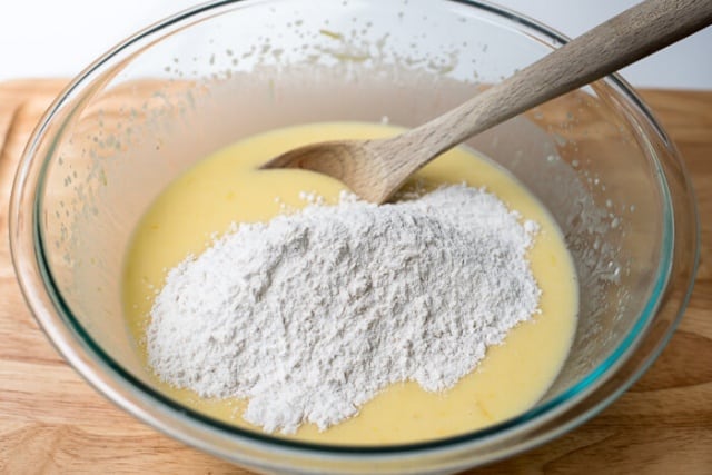Dry ingredients on top of wet ingredients in a mixing bowl with a wooden spoon.