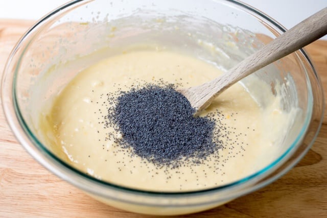 Poppy seeds on top of quick bread batter in a mixing bowl with a wooden spoon.