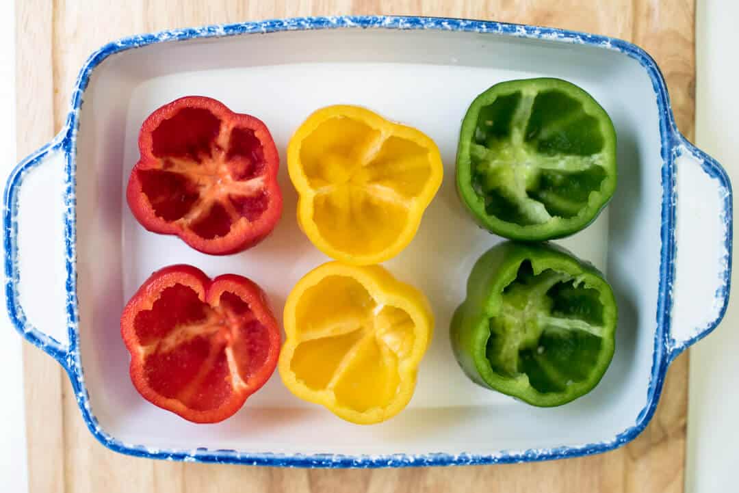 Colorful bell peppers with the tops removed in a baking dish.