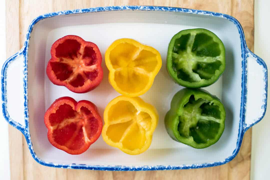 Colorful bell peppers with the tops removed in a baking dish.