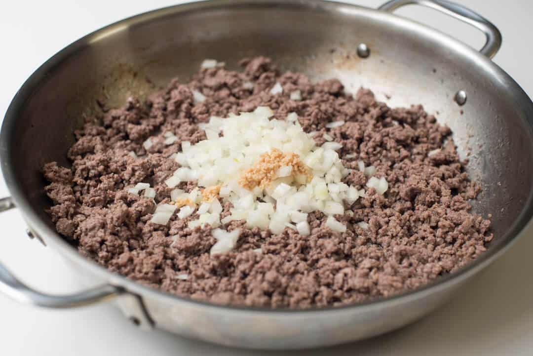 Cooked ground beef in a skillet with onion and garlic.