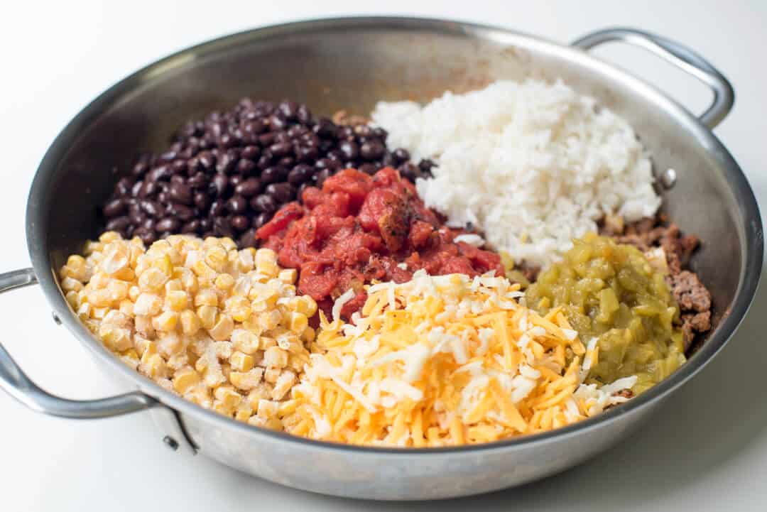 Black beans, rice, tomatoes, frozen corn, diced green chiles, and shredded cheese in a skillet.