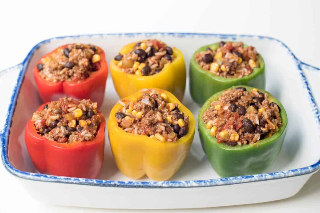 Bell peppers stuffed with a Mexican ground beef filling in a baking dish.
