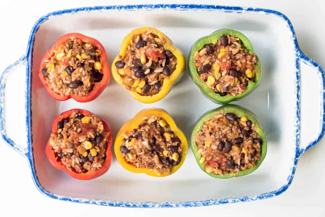 Bell peppers stuffed with a Mexican ground beef filling in a baking dish shot from over the top.