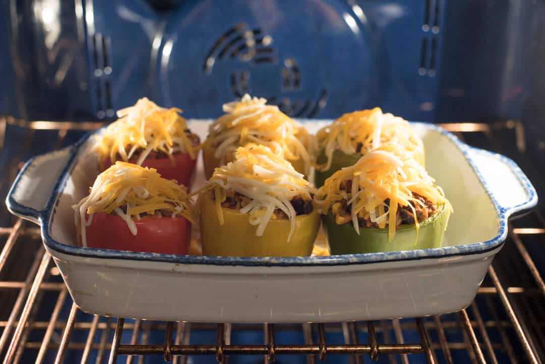 Mexican Stuffed Peppers topped with shredded cheese in a baking dish in the oven.