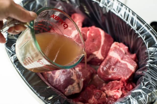 Beef broth pouring into a slow cooker full of beef.