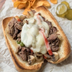 A hoagie roll with shredded beef, peppers, and melted cheese on parchment paper.