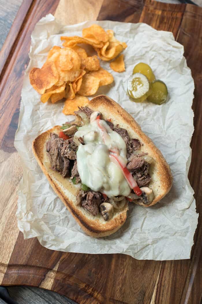An over the top shot of a drip beef sandwich with potato chips and pickles next to it.
