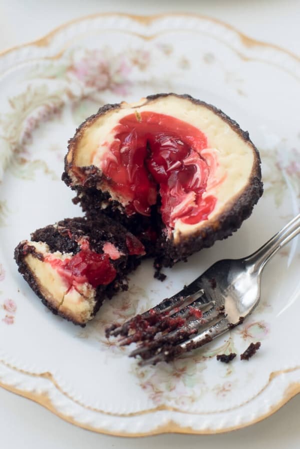 A close up of a fork resting on a pretty china plate with a Cherry Cheesecake Brownie Cupcake.