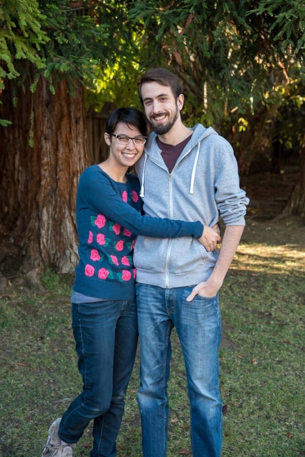 A young woman and man standing on grass in front of trees.