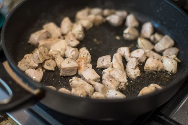 Pieces of chicken in a skillet with oil.