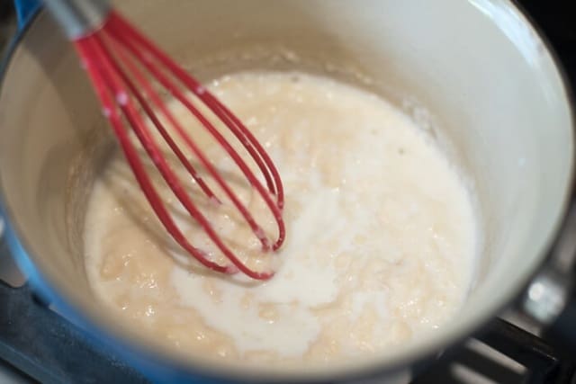 Flour, butter, and milk, being whisked in a saucepan.