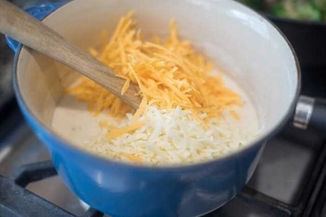 Shredded cheese on top of white sauce in a blue saucepan.