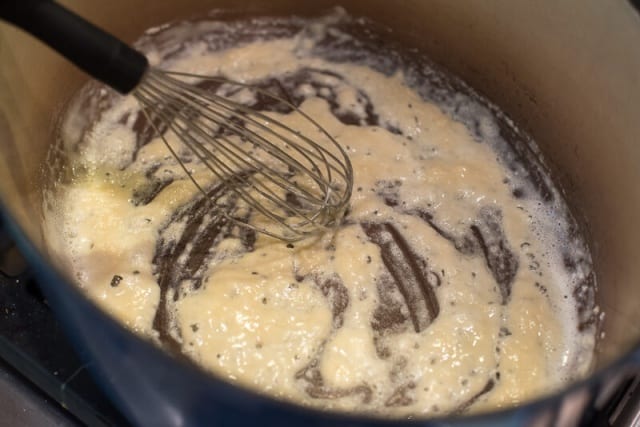 A whisk combining melted butter and flour in a Dutch oven.