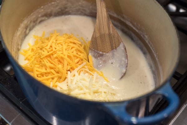 Shredded cheese in a Dutch oven with a white sauce and a wooden spoon.
