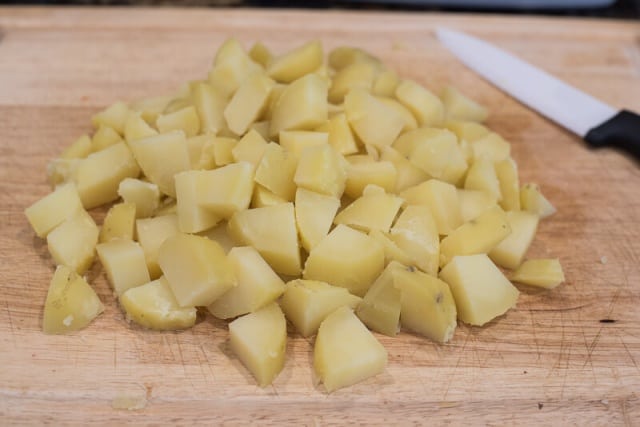 Chopped cooked potatoes on a cutting board.