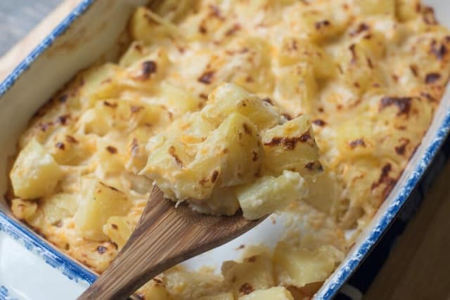 A wooden spoon scoops Au Gratin Potatoes from a blue and white baking dish.
