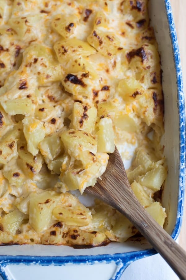 A close up of a wooden spoon scooping Au Gratin Potatoes in a blue and white baking dish.