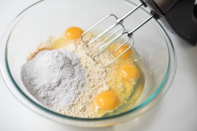 The cake mix, pudding mix, eggs, and vegetable oil are combined with a hand mixer in a glass bowl.